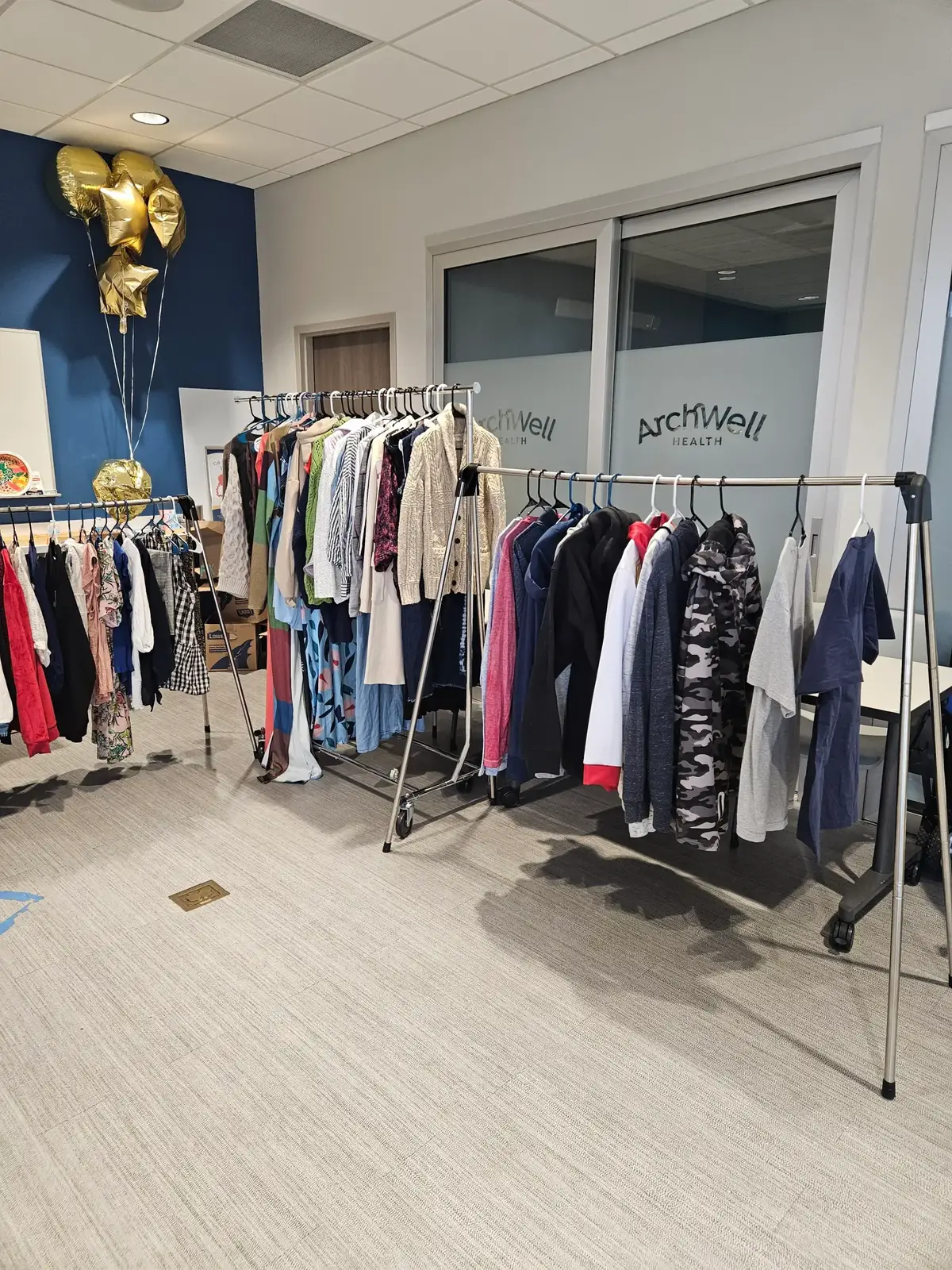 Wide room view with clothing racks, gold balloons, and ArchWell Health signage at the Senior Clothes Closet